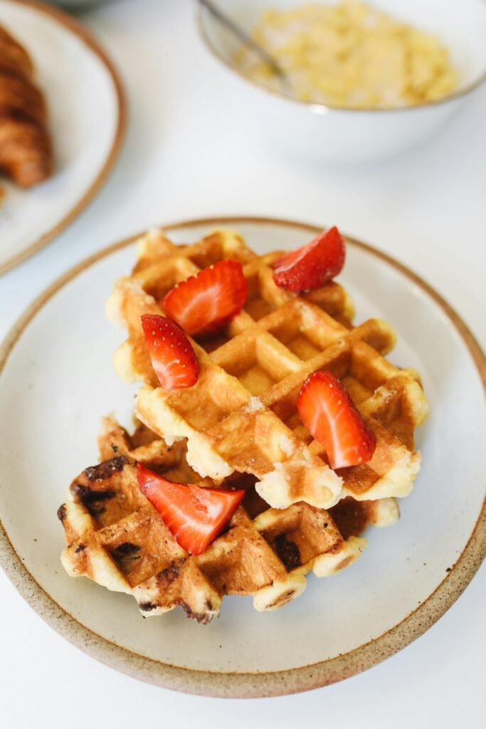 Golden waffles topped with fresh strawberries on a white plate, perfect for breakfast.